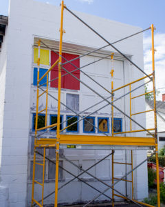Mid-progress of mural project. Marquette artist Taryn Okesson uses scaffolding to reach the top of the mural. Mondrian Garage Mural Third Street, Marquette, MI.